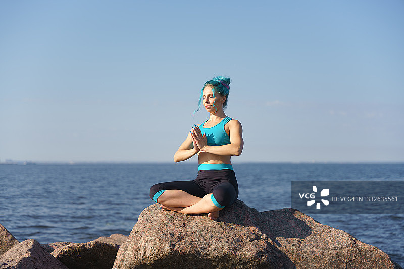 穿着蓝绿色瑜伽服的有魅力的年轻女子在石头上闭着眼睛双手合十图片素材
