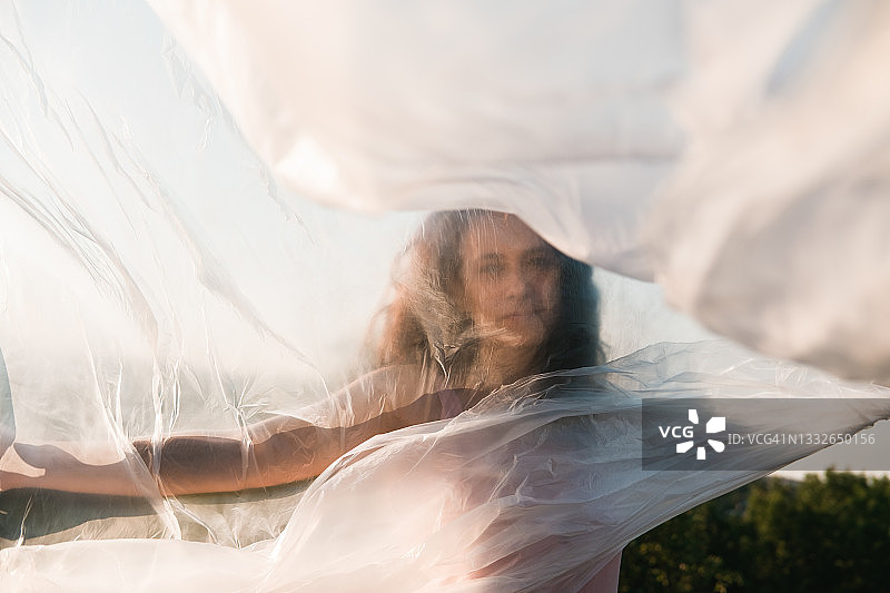 年轻女人站在草地上，手持透明玻璃纸随风飘动图片素材