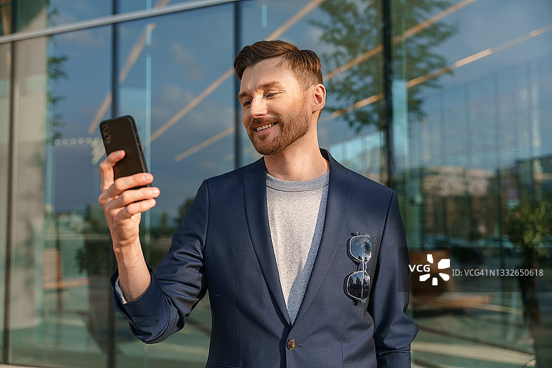 一位穿着灰色T恤和蓝色西装的年轻红发企业家正在阅读手机上的消息图片素材