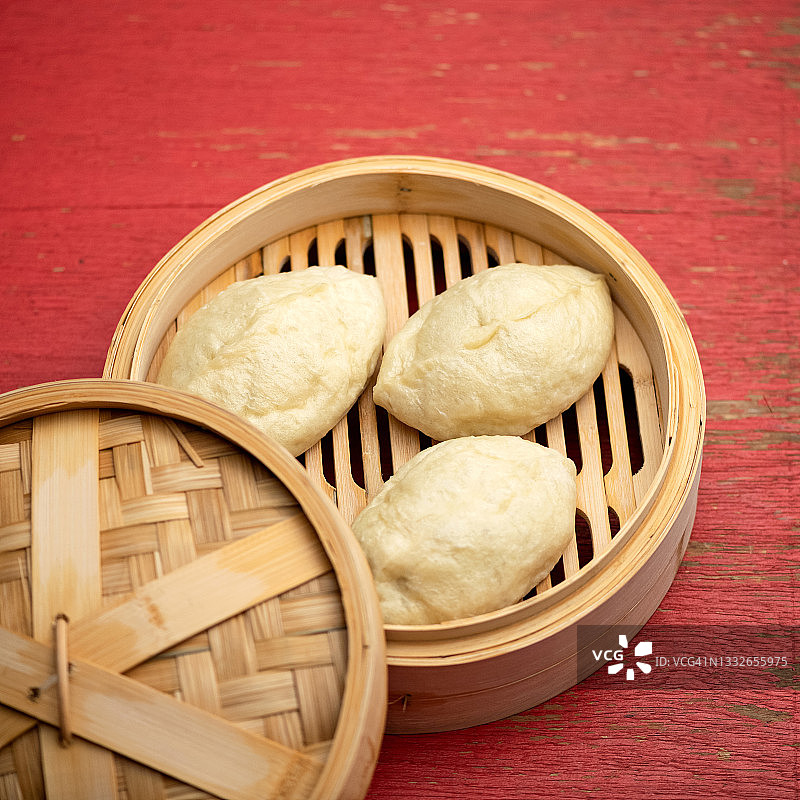 中式美食：烹饪面包，木制筛子或篮子上的生面团，粉色木质背景竹蒸笼上的未煮熟的包子，虚焦特写图片素材