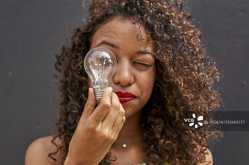 年轻的非洲裔卷发女人穿着绿色露脐上衣，在黑墙前拿着灯泡图片素材