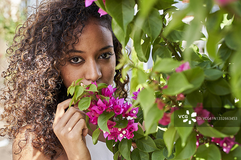 有着卷发和棕色眼睛的年轻非洲裔女人拿着粉色花朵摆姿势图片素材