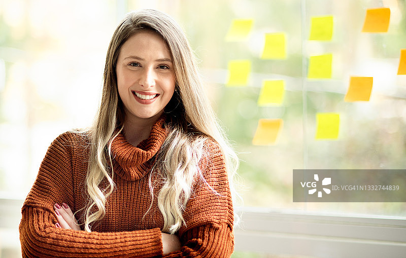 在办公室的窗户上用便利贴进行头脑风暴的微笑年轻女商人图片素材