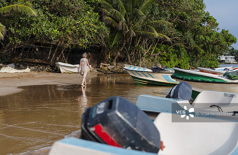 在停泊着摩托艇的热带海滩附近行走的中年妇女图片素材