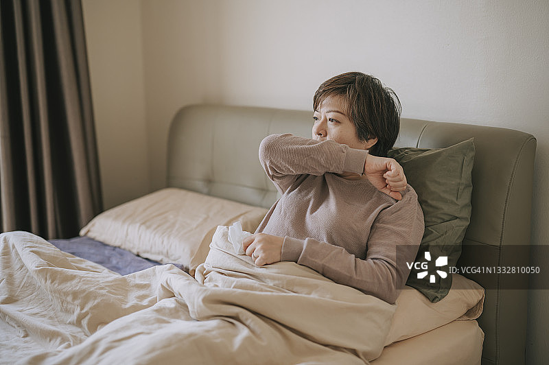 亚洲华人中年妇女咳嗽到手肘不舒服生病在家卧室休息图片素材