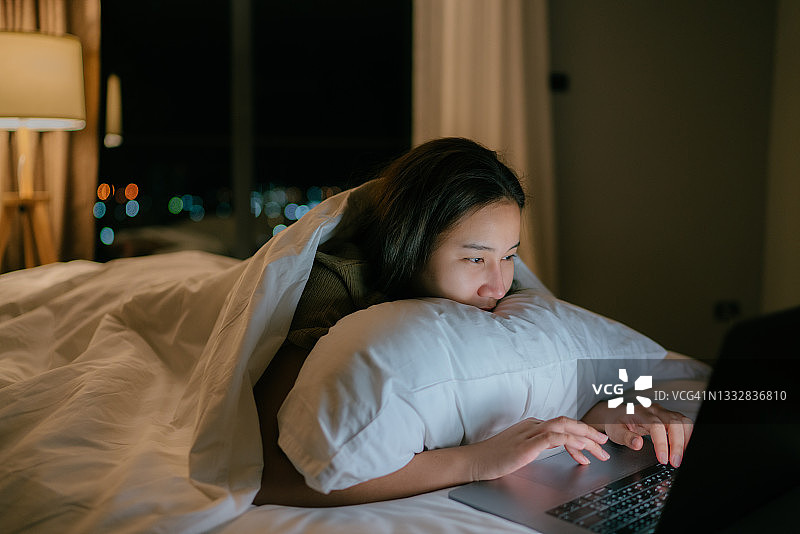 年轻女人躺在床上使用笔记本电脑图片素材