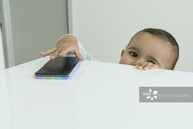 一个2岁的男孩看着镜头，顽皮地拿着他母亲的手机图片素材