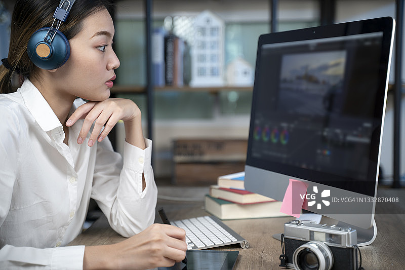 戴着耳机在电脑上进行视频编辑图片素材