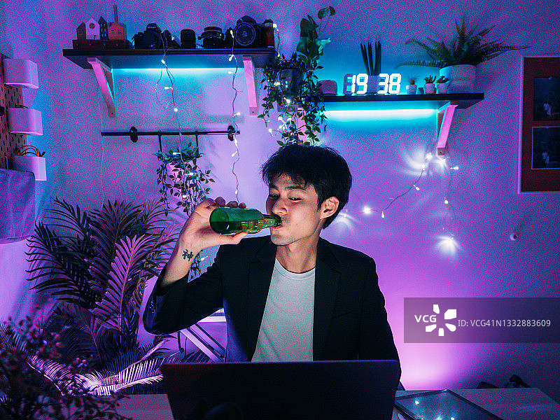 亚洲男子在家参加视频会议时喝啤酒图片素材