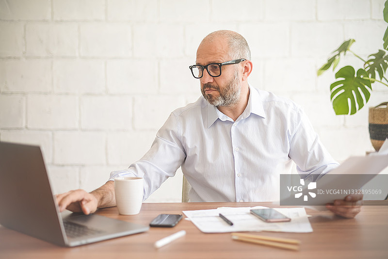 在办公室工作的成熟男人（使用笔记本电脑，处理文书工作）图片素材