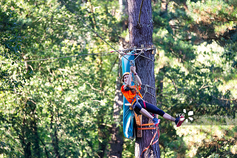 快乐的少女在自然中的滑索公园里沿绳索滑下，面带微笑图片素材