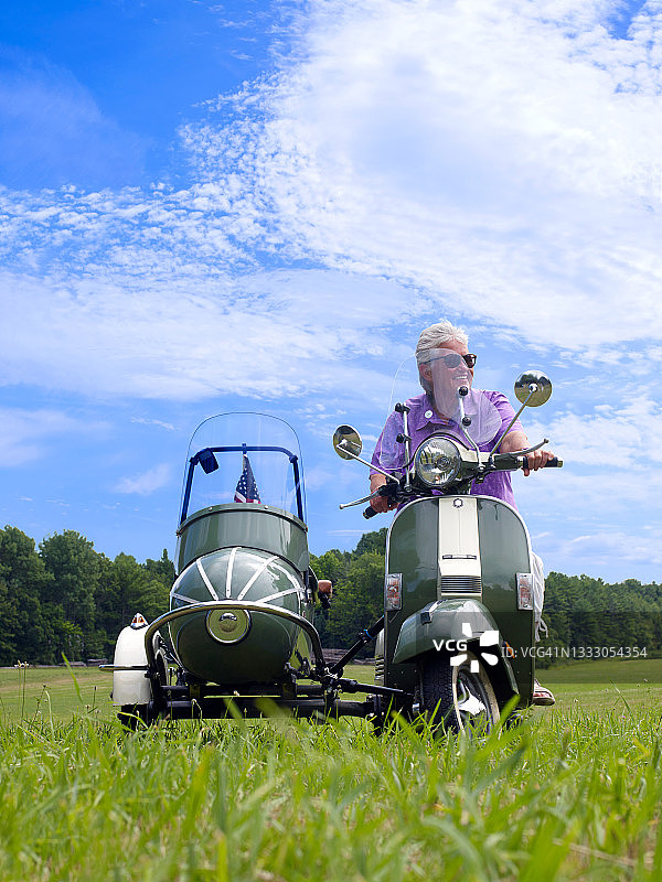 在紫色衬衫上的微笑女人，在田野里用侧车踏板车图片素材