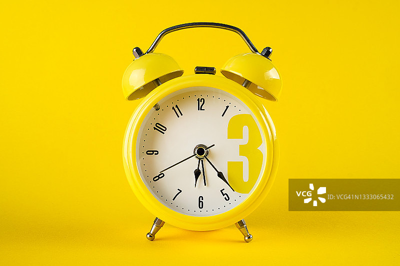 亮黄色背景上的复古铁制闹钟，留白区域图片素材