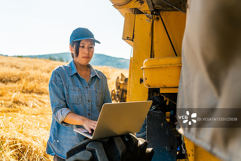 女性农民坐在联合收割机上使用笔记本电脑图片素材