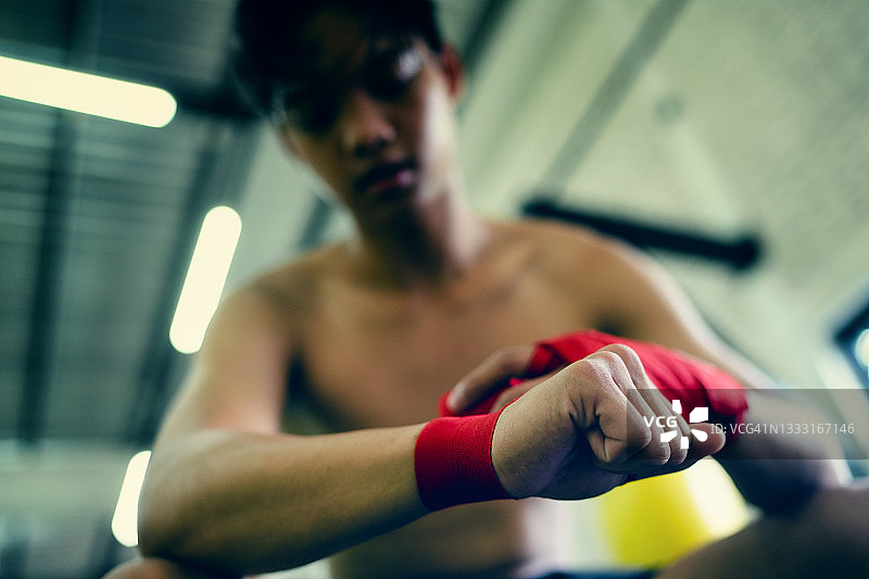 健身房里充满斗志的亚洲青少年业余拳击手，准备用红色拳击绷带缠手图片素材