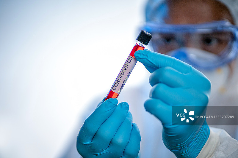 新冠病毒：医生、护士、科学家穿着防护服戴着口罩，手持受污染的患者血液样本试管， SARS-Cov-2病毒检测呈阳性图片素材