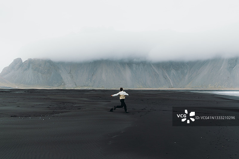 年轻女游客在黑沙滩上欣赏山景图片素材