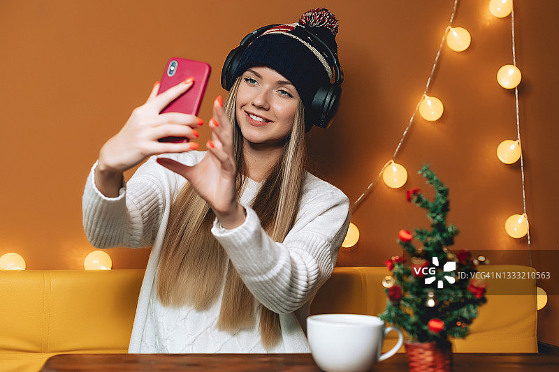 戴着美国帽子，用智能手机自拍的漂亮女人们，圣诞树在木桌上图片素材