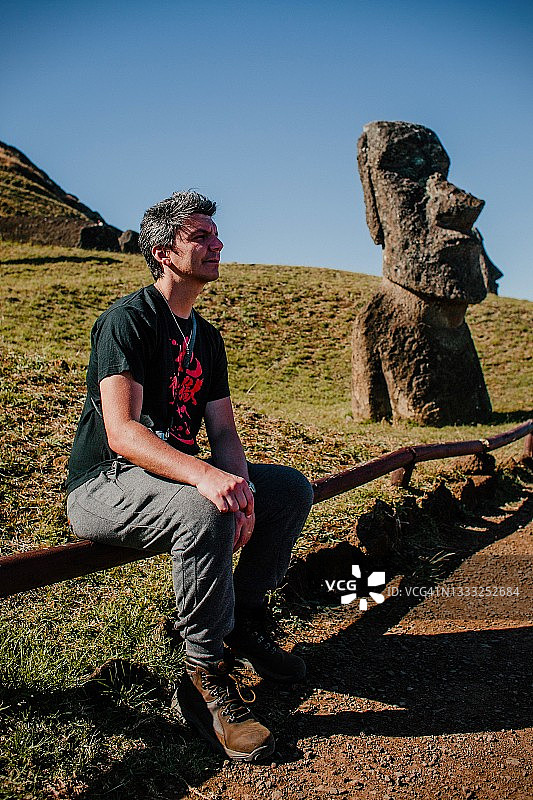 在智利复活节岛采石场，坐在莫埃雕像前的白人男子图片素材