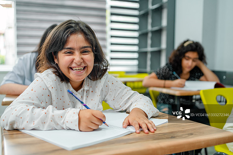 坐在教室书桌前对着镜头微笑的小学女生图片素材
