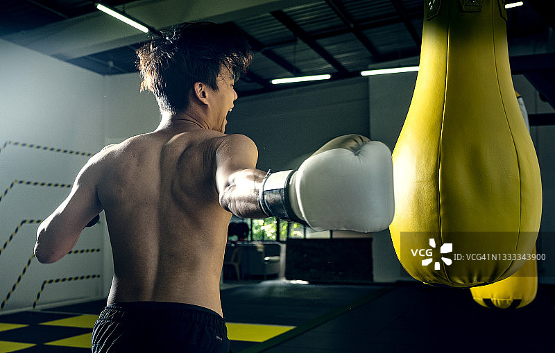亚洲运动型男青少年业余拳击手，充满动力地练习强力勾拳，配有黄色拳击袋图片素材