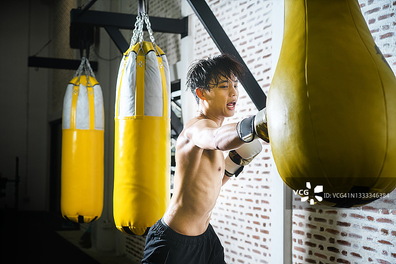 亚洲运动型男青少年业余拳击手，充满动力地练习强力勾拳，配有黄色拳击袋图片素材