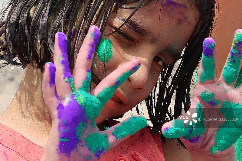 印度教女孩站在洒满颜料的霍利节上，手掌沾满颜料，面部特写，看着镜头图片素材