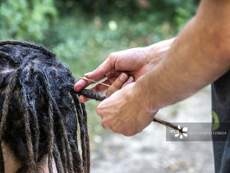 一个留着骇人长发的男人，在大自然中与理发师一起在户外做发型。图片素材