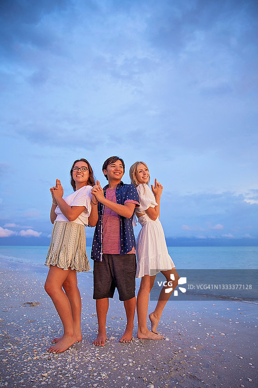 三个兄弟姐妹在海滩上摆出滑稽的姿势图片素材