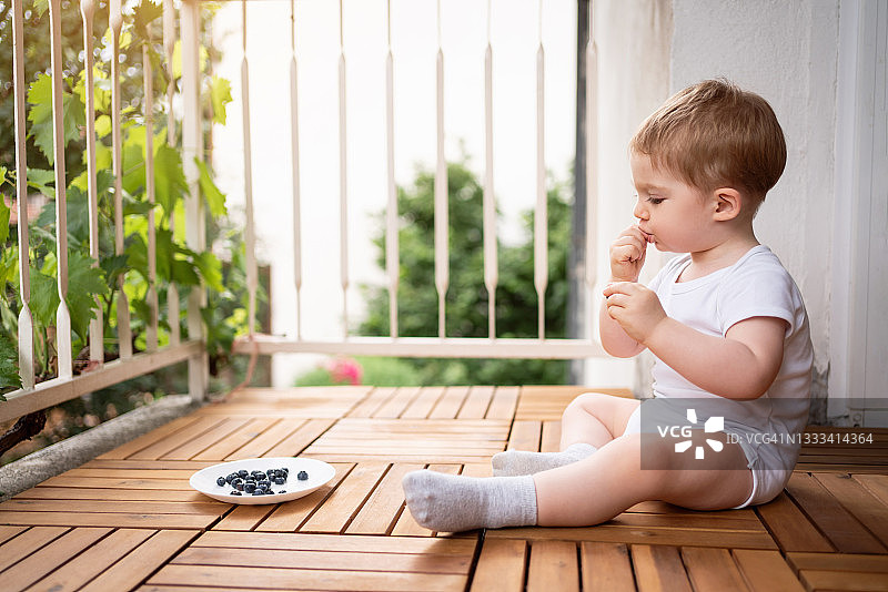 坐在阳台上吃蓝莓的可爱小男孩侧视图图片素材