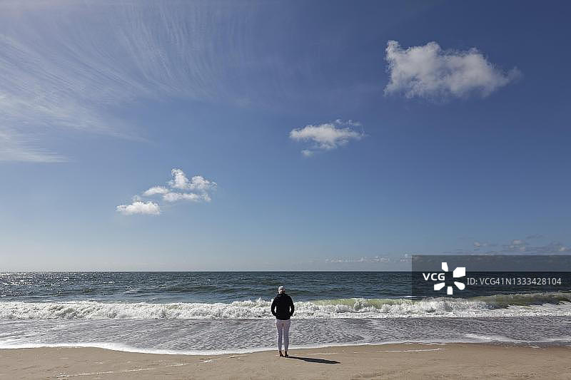 在海滩上眺望大海的连帽衫单人，位于德国石勒苏益格-荷尔斯泰因州叙尔特岛北弗里西亚群岛图片素材