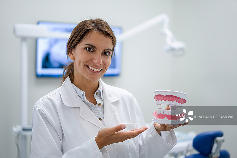 诊所里拿着假牙微笑的快乐牙医图片素材