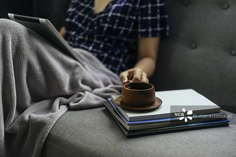 年轻成年女性坐在舒适的沙发床上，在家放松地端着木杯咖啡图片素材