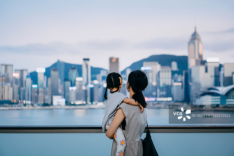 年轻的亚洲母亲抱着女儿，在市中心城区的城市露台上享受亲密的亲子时光图片素材