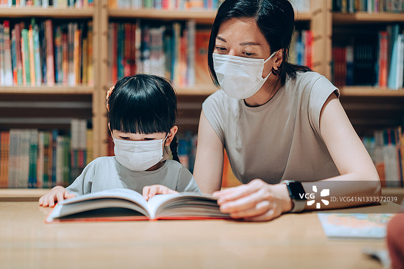 年轻的亚洲母亲和小女儿在图书馆一起读书图片素材