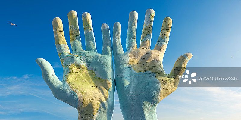 两只手一起举起绘制的世界地图，以蓝色天空为背景图片素材