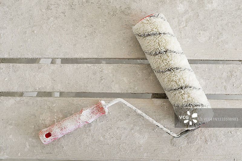 木桌或梯子上沾满白色油漆的建筑滚筒，房屋建造或公寓维修工具图片素材