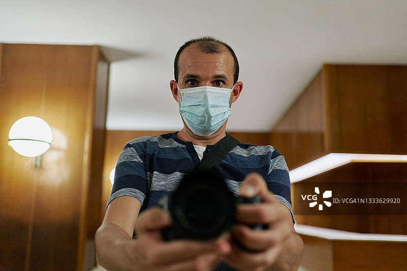 在室内戴着口罩用数码相机拍照的站立男子图片素材