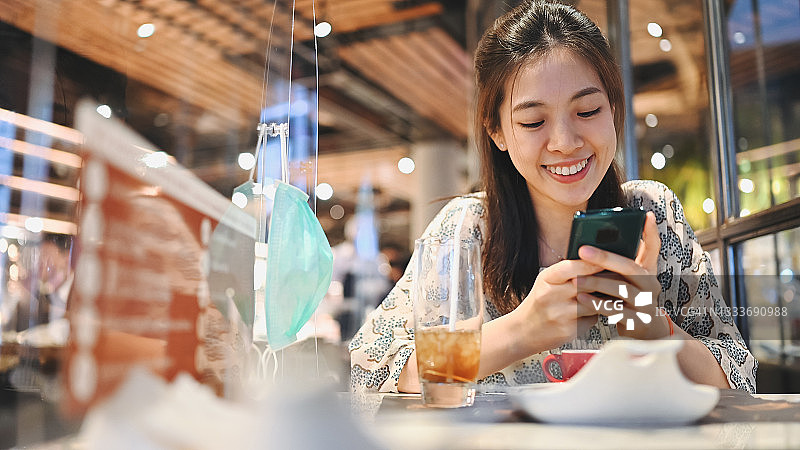 亚洲成年女性戴着口罩享受美食，并通过手机享受社交媒体图片素材