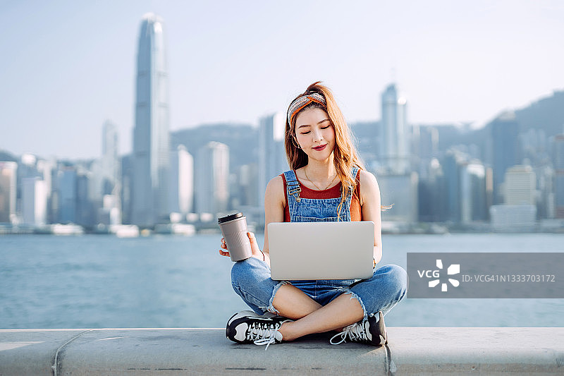 年轻亚洲女性在海滨长廊用笔记本电脑图片素材