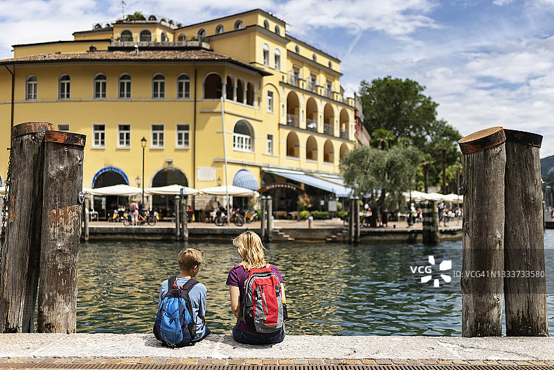 母亲和儿子坐在加尔达里瓦的港口欣赏城镇和湖泊的景色图片素材
