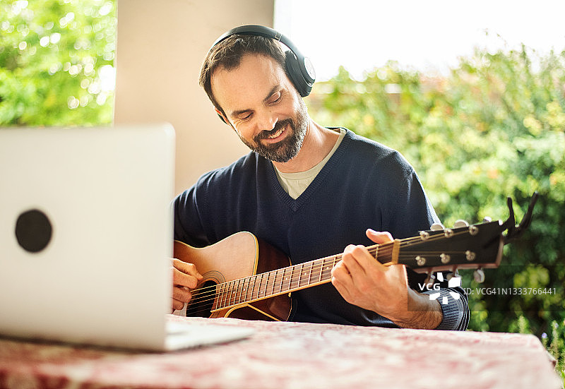 戴着耳机在露台上进行在线吉他课程的微笑男人图片素材