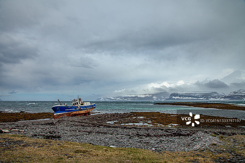 戏剧性天空下的沉船和峡湾海岸线上覆盖着海藻和岩石的海滩的广角镜头图片素材