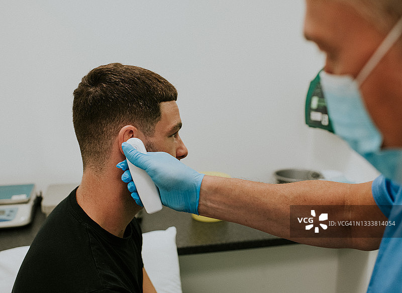 医护人员使用红外耳温枪为男病人测量体温图片素材