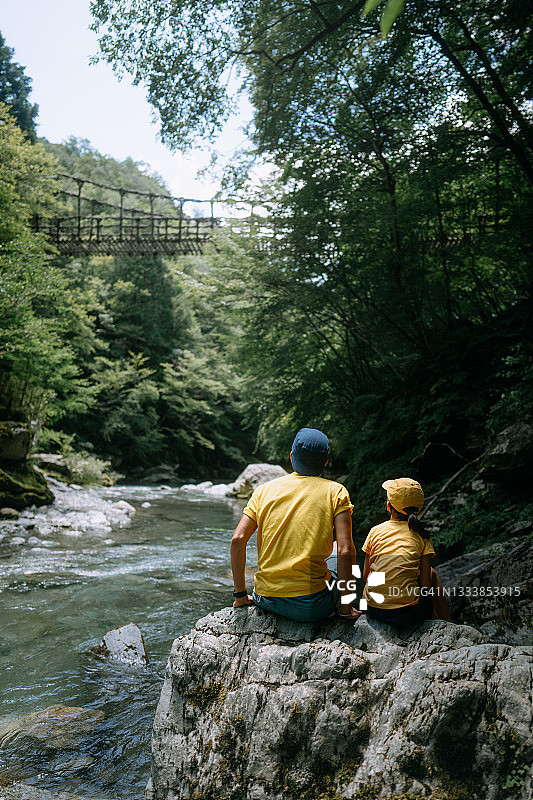 年轻女孩和父亲坐在河边，日本伊亚山谷图片素材