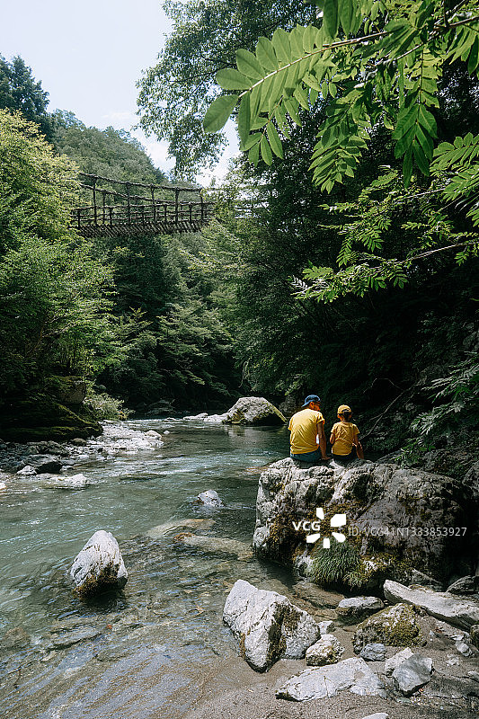 年轻女孩和父亲坐在河边，日本伊亚山谷图片素材