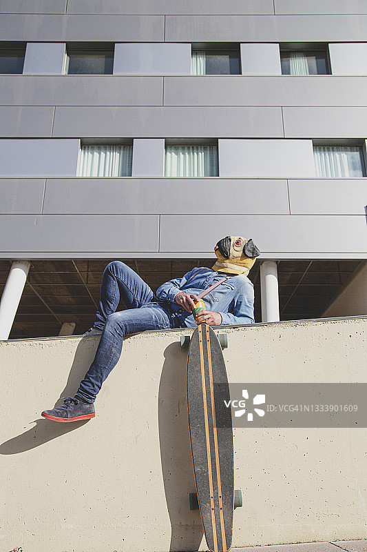 戴着哈巴狗面具的男人躺在墙上支撑着长板图片素材