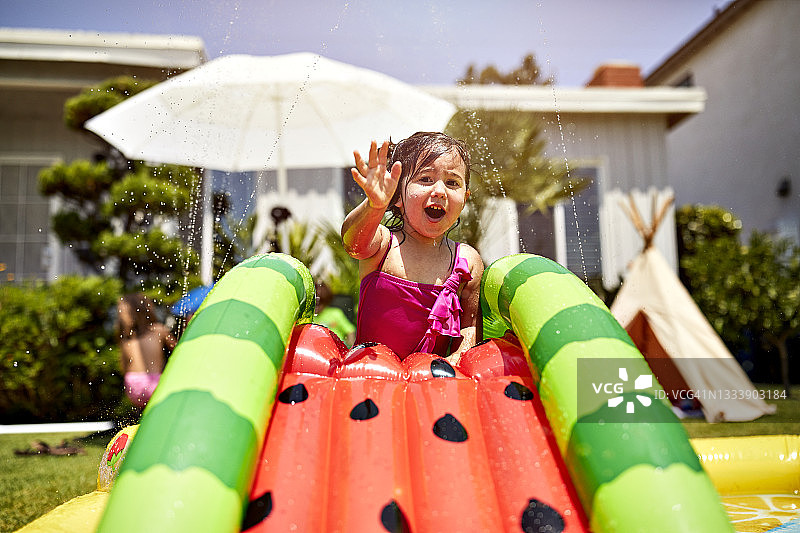 女孩在后院潮湿的充气滑梯上玩耍图片素材