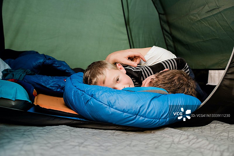 男孩在家庭帐篷里露营时拥抱睡袋里的爸爸图片素材
