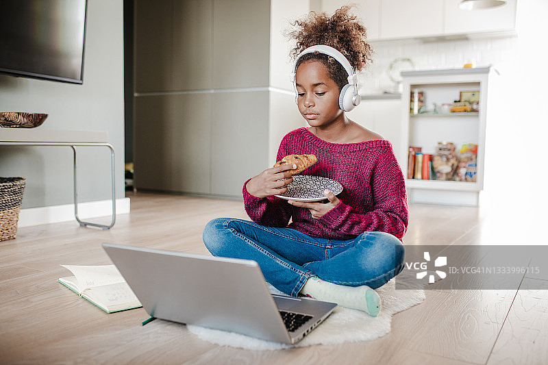 非裔美国小女孩在家使用笔记本电脑并吃早餐图片素材